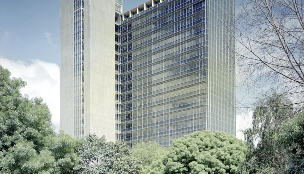 Large concrete and glass building standing above the trees on a sunny day