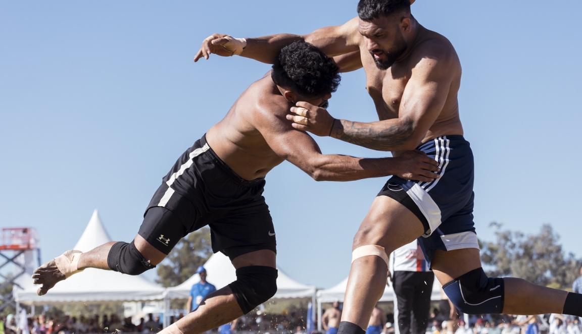 Two men in a Kabaddi match outside on a cloudless day