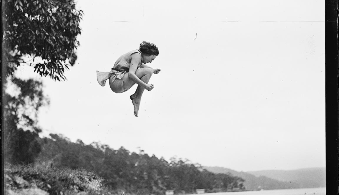 Black and white photo young woman leaping in the air with her knees tucked up to her chin