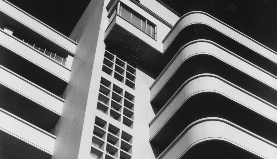 Black and white photo looking up at a building with curved balconies and lot's of small square windows