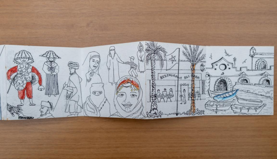 Fold-out travel diary open to three pages with black and white illustrations of Moroccan people and streets