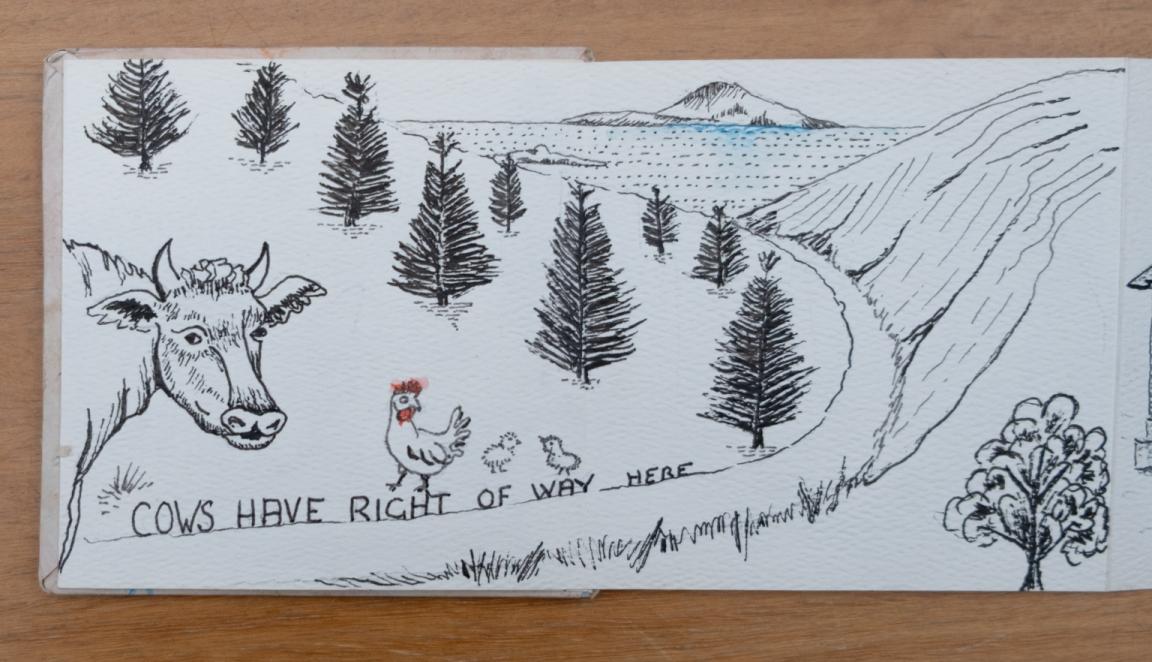 Fold-out travel diary open to four pages with black and white illustrations of a cow and a chicken on a road going between mountains towards the sea and text reading 'Cows have right of way here'