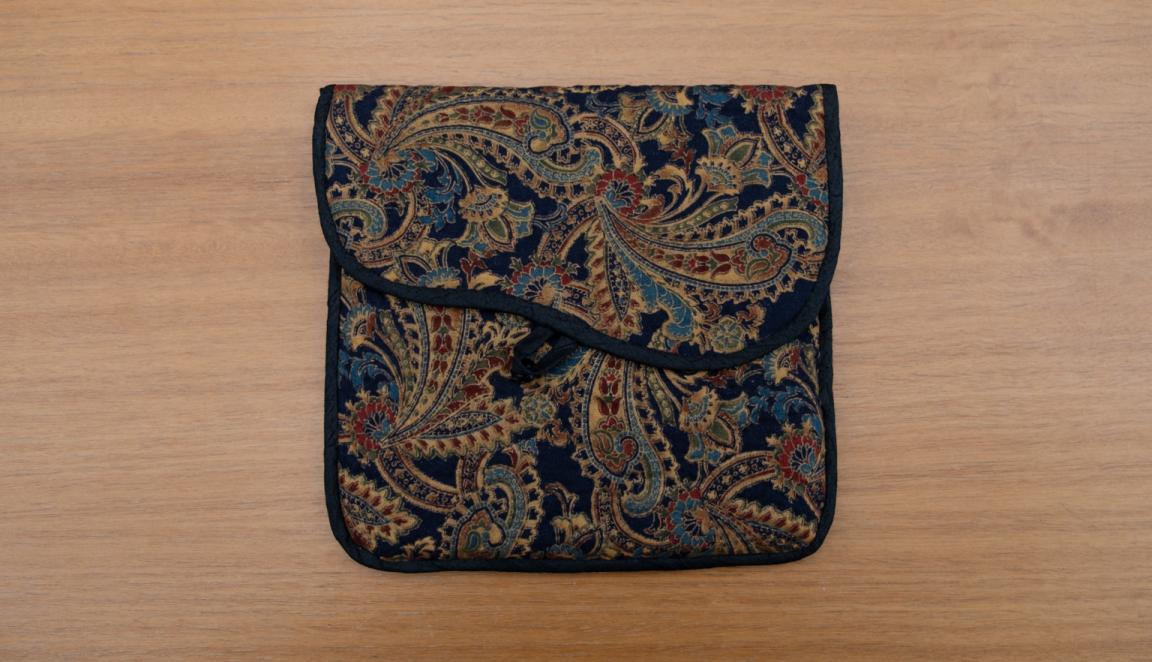 Fabric slipcase made of dark material with a paisley-like pattern in gold and dark jewel-tones