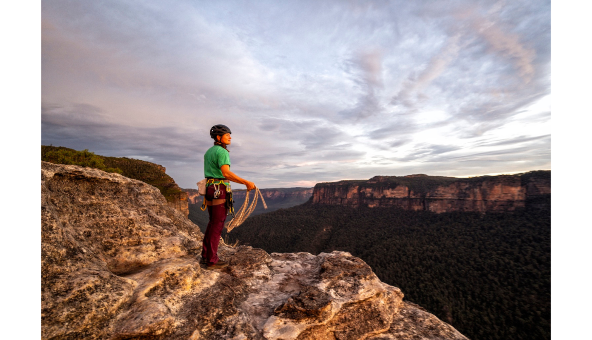 Female mountain climber standing at the top of a cliff, looking out at a beautiful dusk over the Blue Mountains
