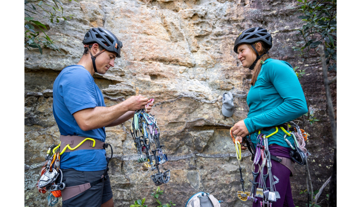Two mountain climbers preparing their equipment in front of a rock wall