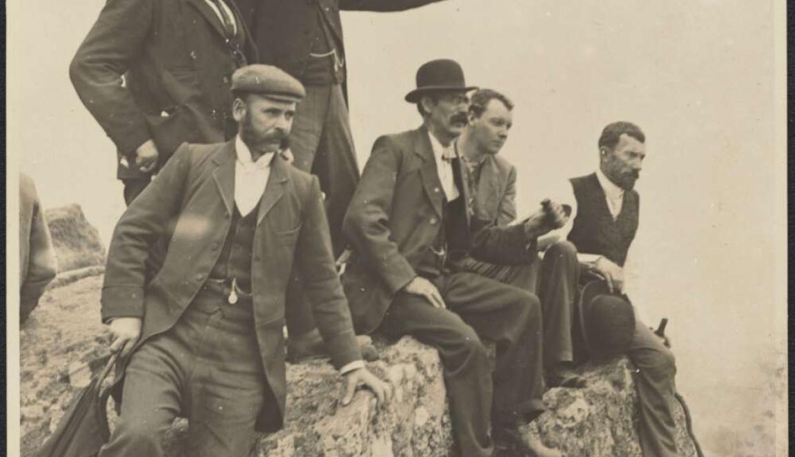 A black and wihte photo of a group of men sitting on a rock and looking over a field