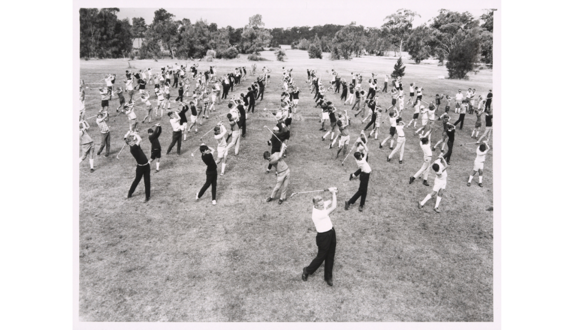 A black and white photograph showing a large group of people practicing a golf swing