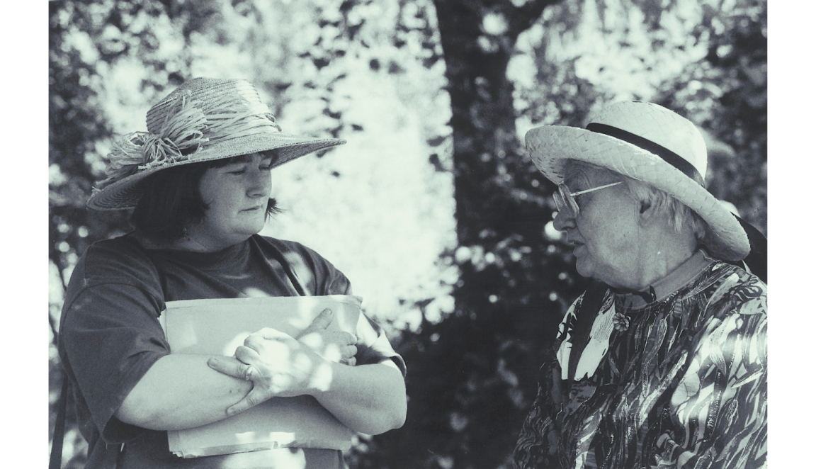 Black and white photo of a younger woman, Jackie French, and an older woman, Judith Wright, standing and talking amongst trees