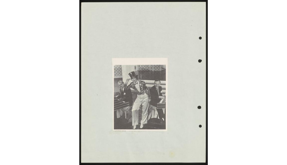 Image of Eleanor Powell wearing sparky jacket and top hat. Seated at keyboards behind her is Arthur Freed and Nacio Herb Brown