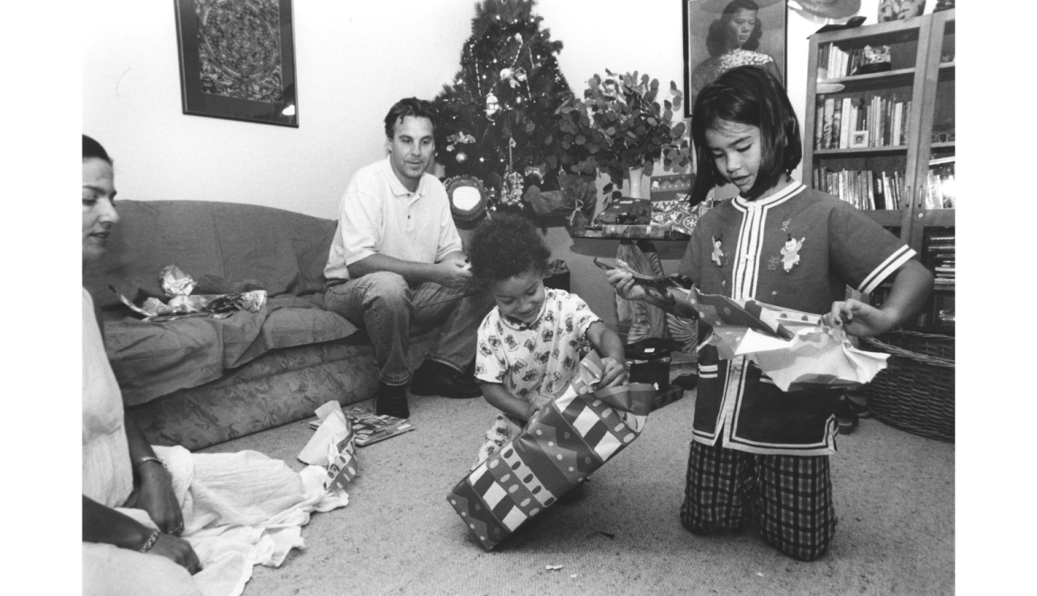 Black and white photo of two children opening Christmas presents, with two adults watching on