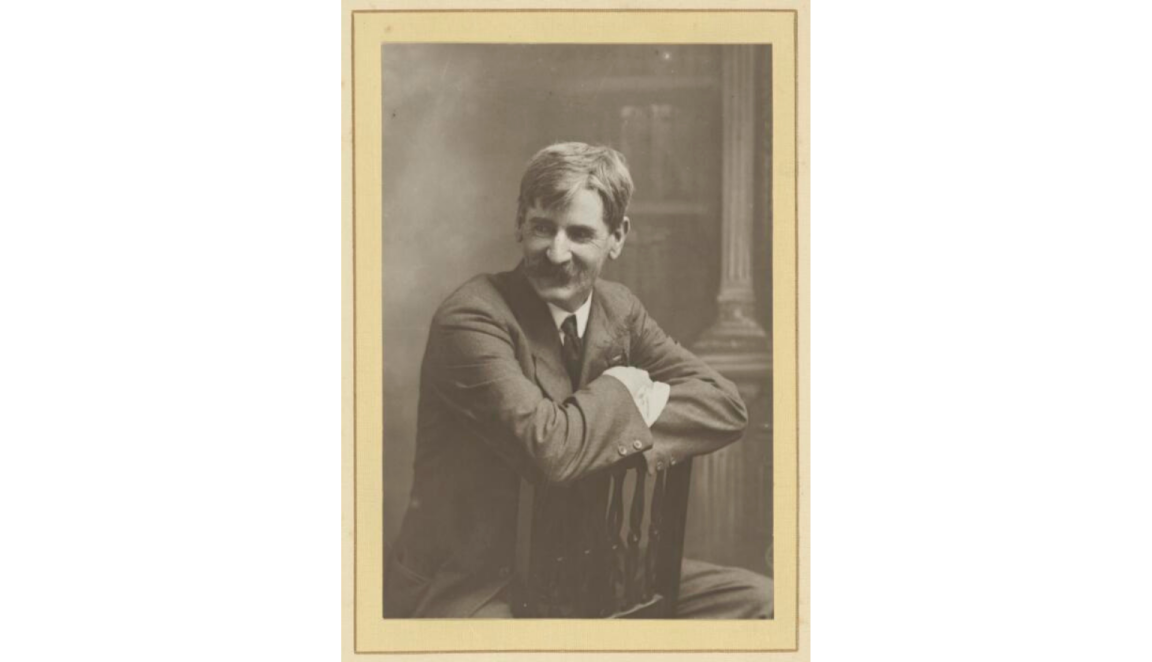 Black and white picture of Henry Lawson seated reverse on a chair, looking to the left off camera