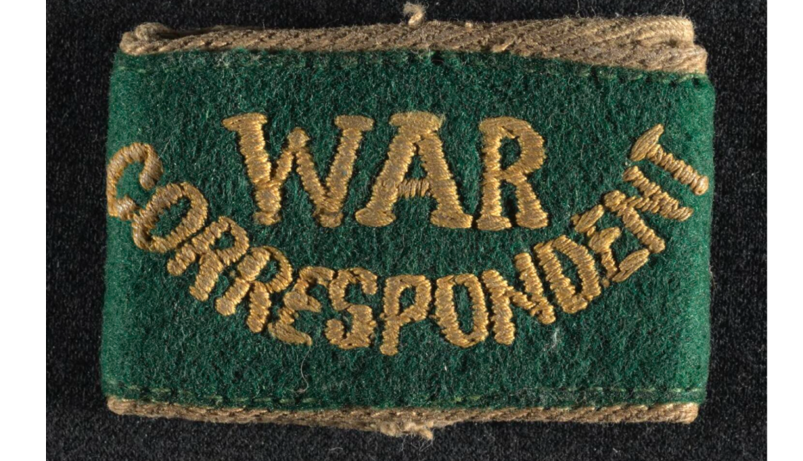 Photograph of green cloth badge, gold edging, 'War Correspondent' stitched in gold full caps.