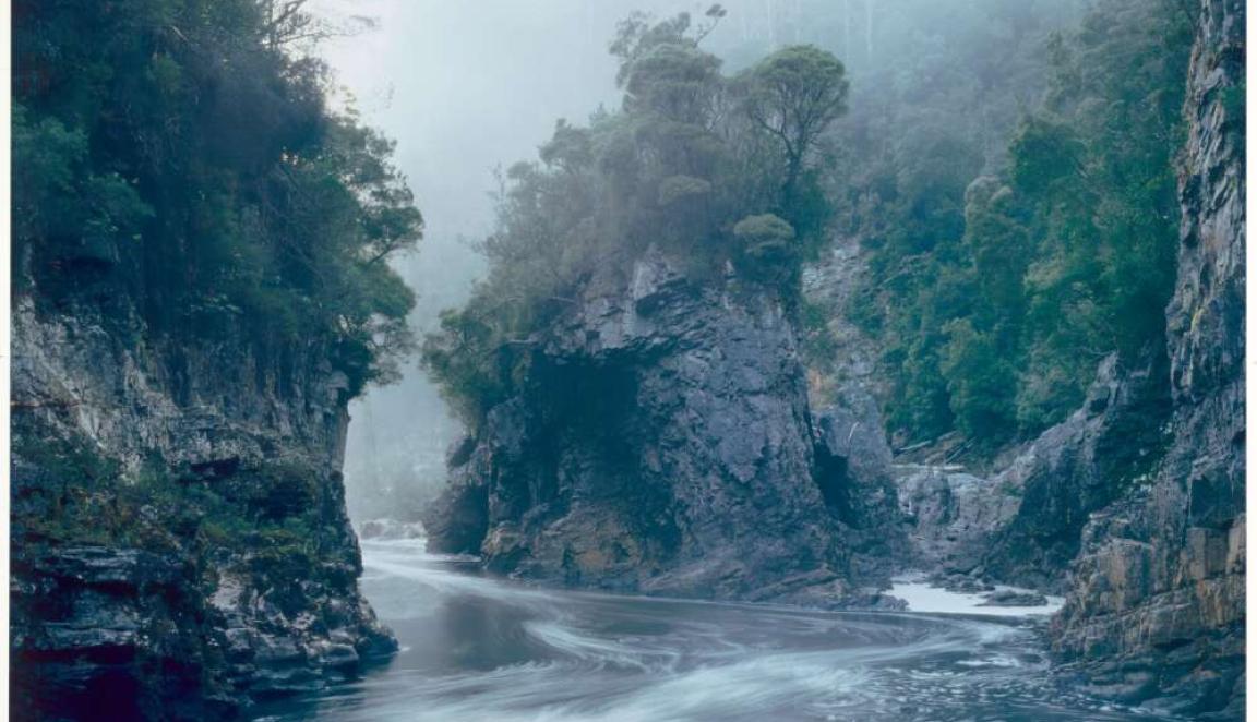 Misty river flowing through a deep, rugged gorge with steep, moss-covered cliffs on both sides.
