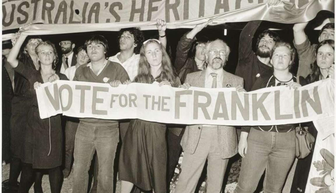 A black and white historical photo of a group of people marching and holding a large banner that reads "NOTE FOR THE FRANKLIN" under a larger banner that says "AUSTRALIA'S HERITAGE".