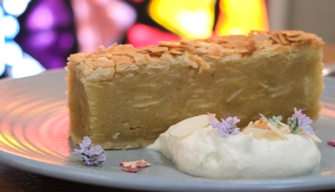 A dessert on a plate with cream and flowers with a colourful stained glass window behind it