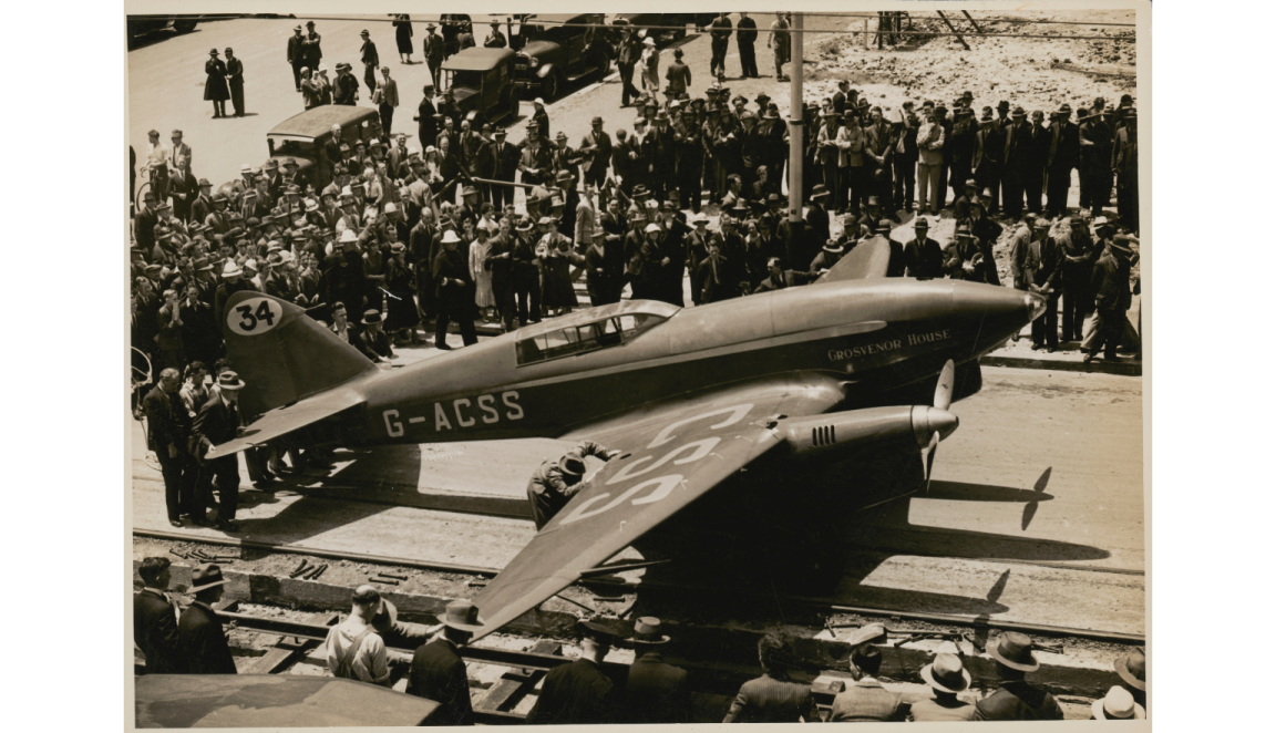 Black and white photo of a crowd around a small black plane
