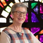 A woman with short hair smiles with stained glass windows in the background