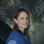 Photo portrait of Katherine Bennell-Pegg, the first Australian astronaut, standing in front of a projection of stars in space