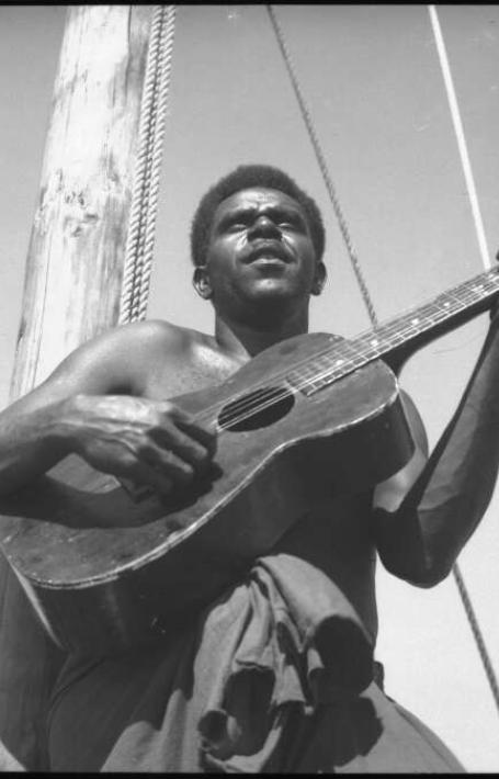 A black and white photo of a man playing a guitar on a boat