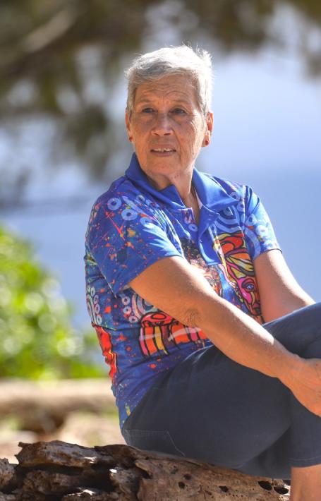 Fijian Australian woman with short grey hair sitting on a rock on a beach