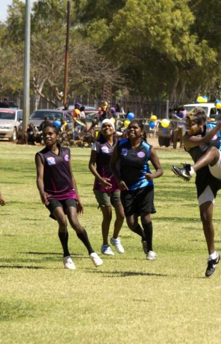 Six women smiling as they play football. One has just kicked the ball.
