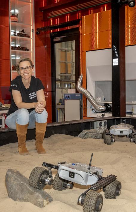 Dr Sarah Cannard sitting on the edge of a sand pit with four space rovers in it