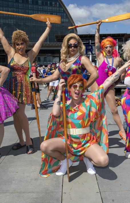 Six drag queens posing with dragon boating paddles on a pier