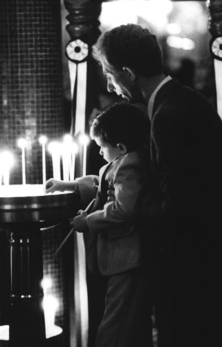Black and white photo of a man helping a young man light candles at a church on Good Friday