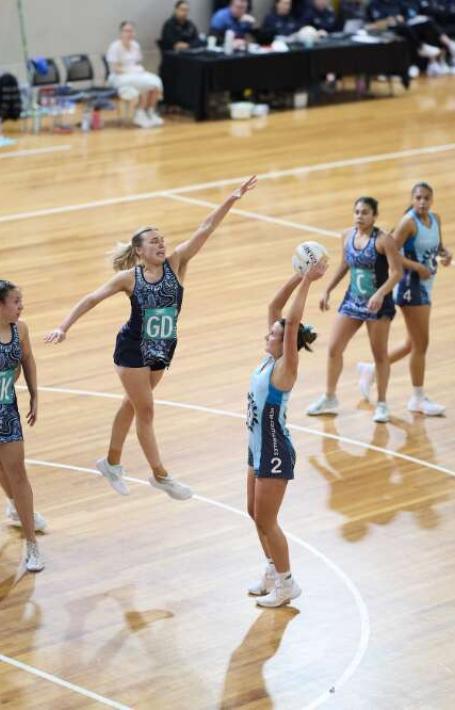 Action shot during a netball game as a women jumps up to prevent another from scoring