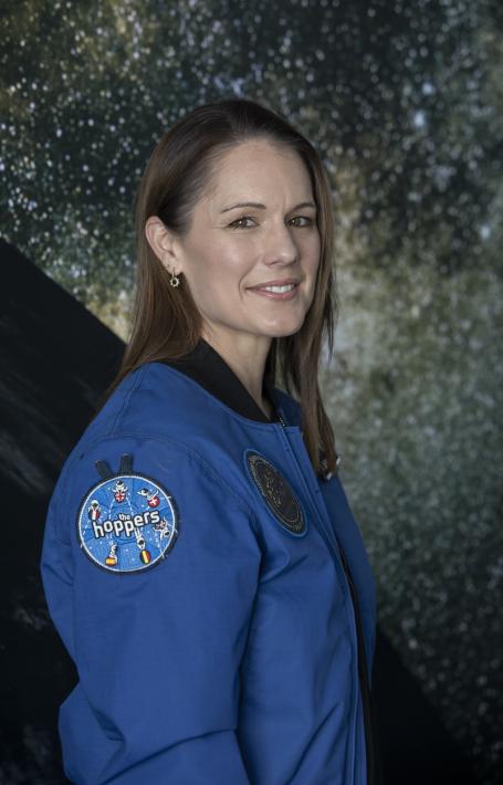 Photo portrait of Katherine Bennell-Pegg, the first Australian astronaut, standing in front of a projection of stars in space