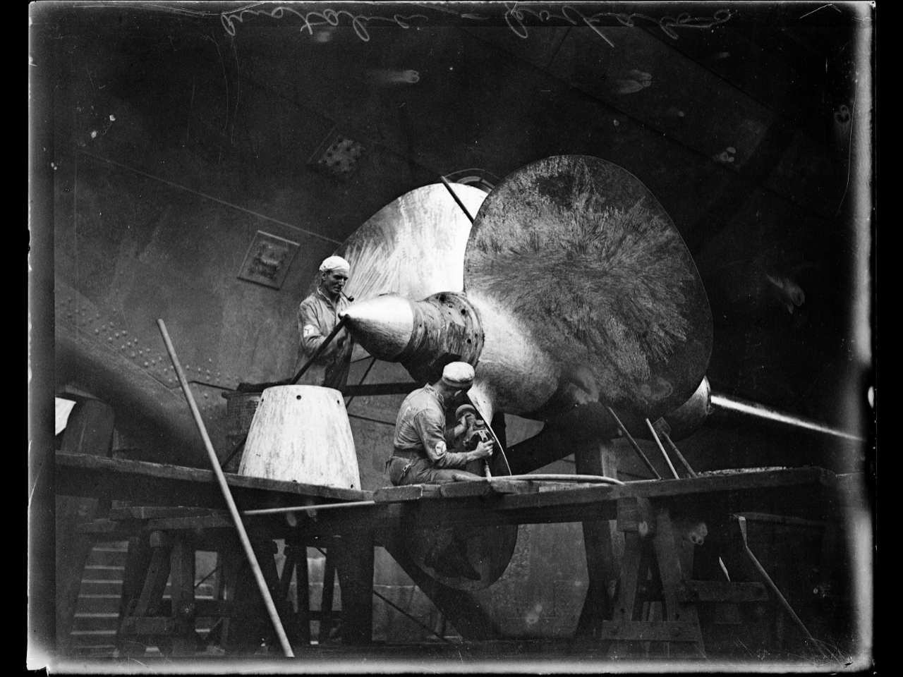 Black and white photo of two men working on a large ship propeller