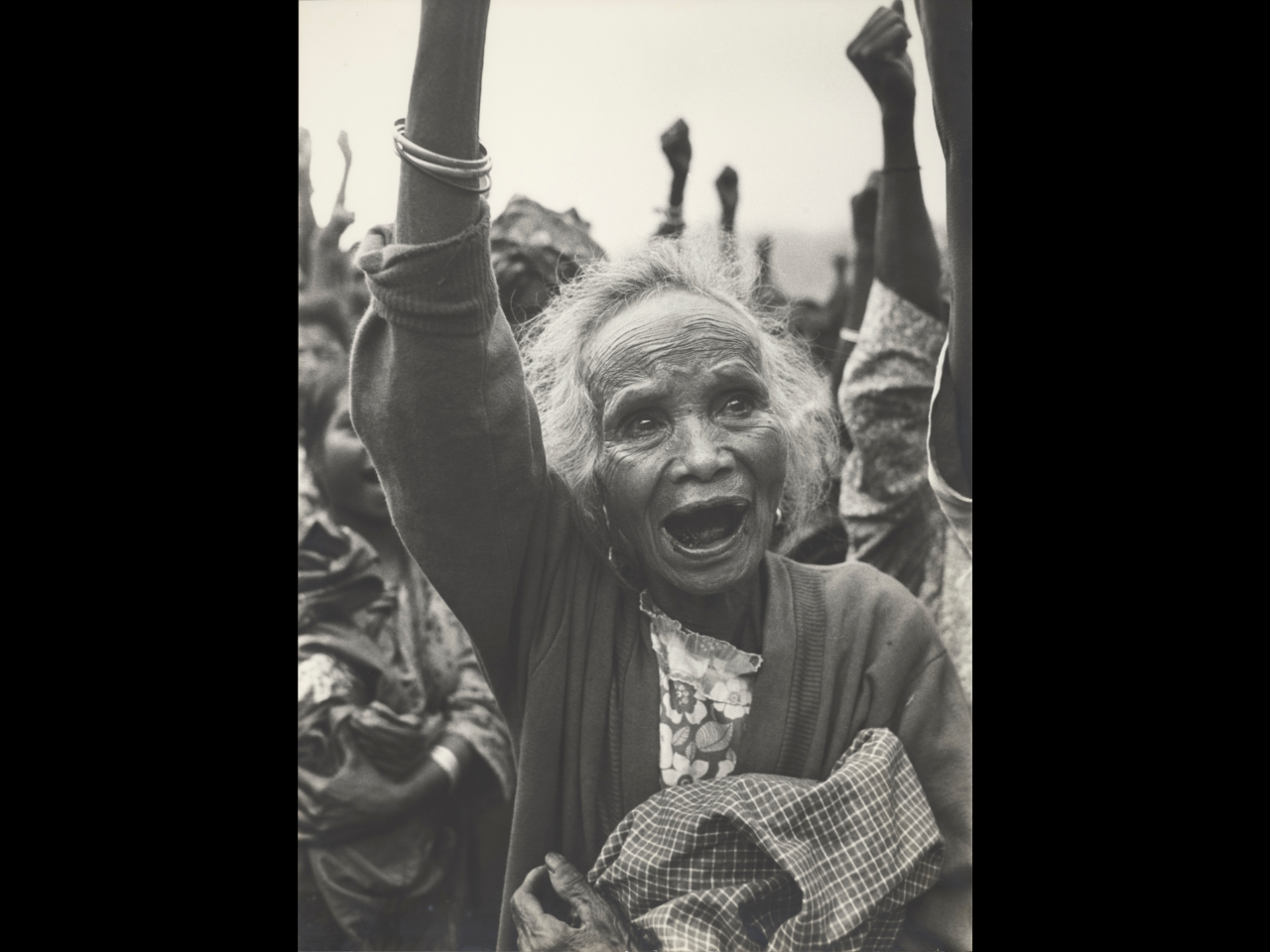 Black and white photo of a female activist in a crowd with everyone raising a fist