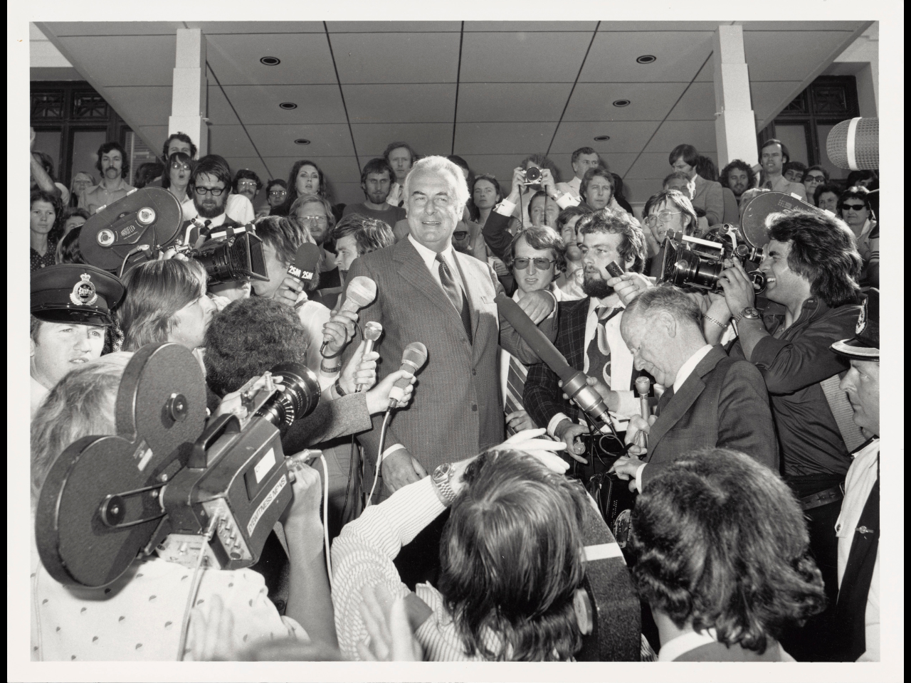 Black and white photo of Gough Whitlam speaking at Parliament House surrounded by reporters