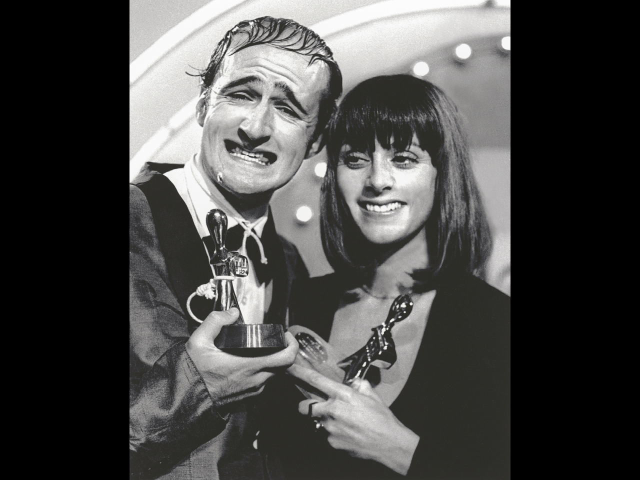 Black and white photo of Norman Gunston and Denise Drysdale smiling and holding up two Logie Awards trophies