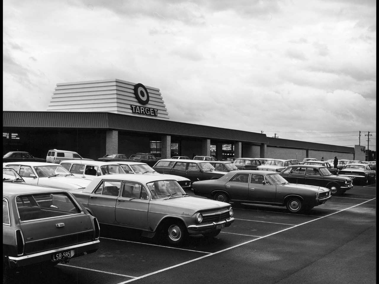 Black and white photo of 1970s cars parked in front of a store
