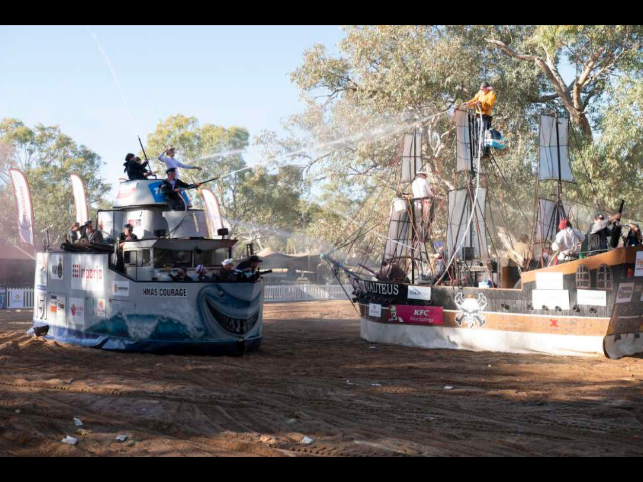 A dynamic scene featuring two large boats engaged in water displays on a dry riverbed. 