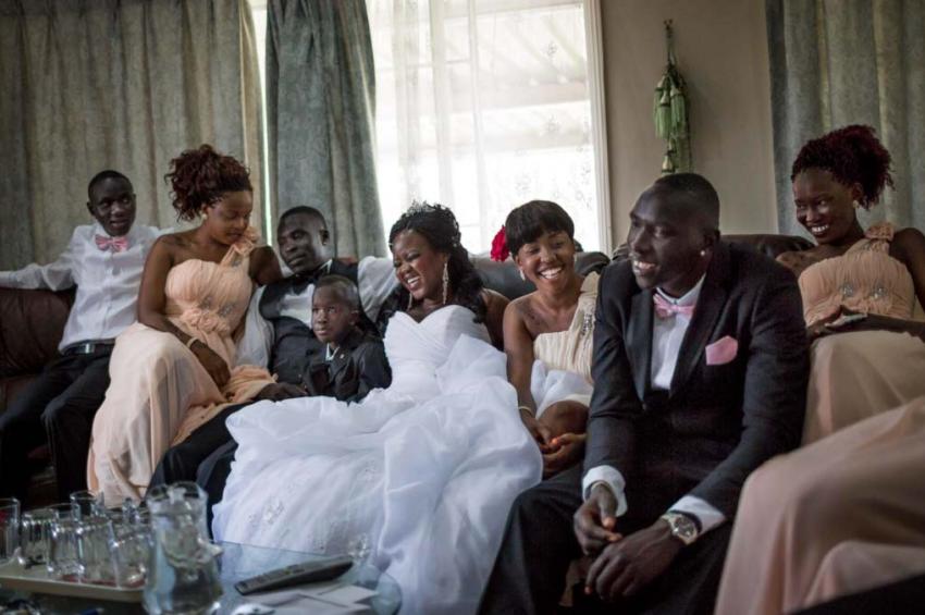 A family dressed for a wedding laughs as they sit together on a couch