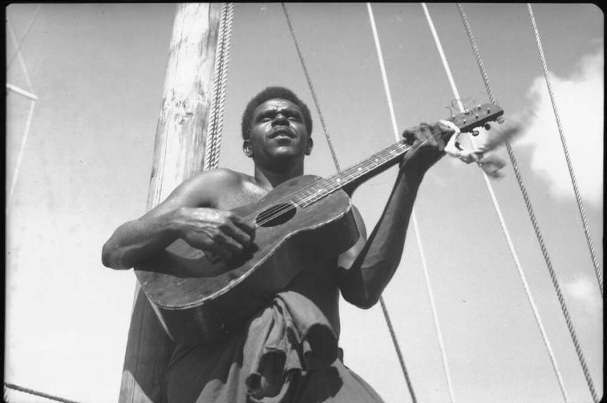A black and white photo of a man playing a guitar on a boat
