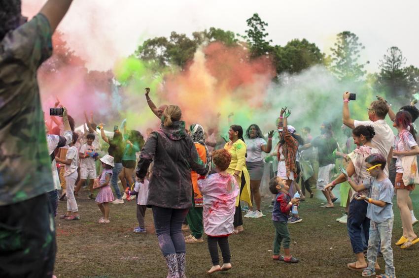 Adults and children in a park throwing gulal, colourful powders, in the air