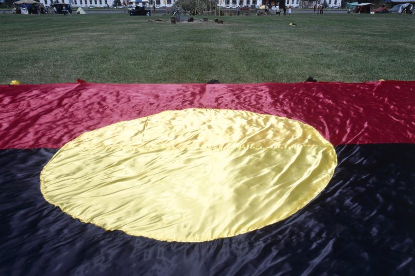 Very large Aboriginal flag laid on the grass in front of Old Parliament House