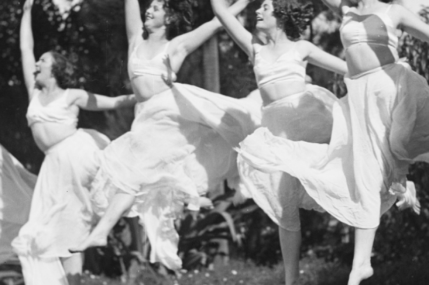 Black and white photo of dance students in white tops and skirts leaping
