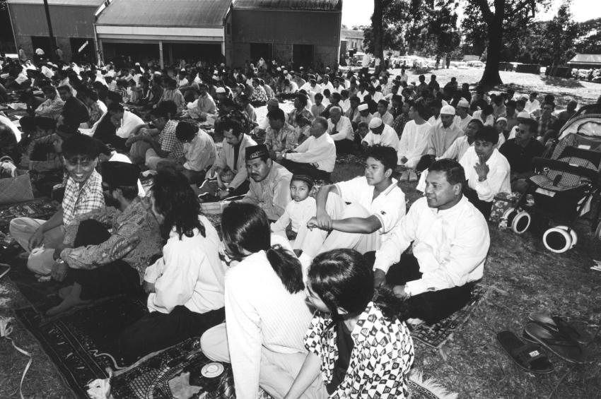 Black and white photo of people of all ages sitting on the ground outside
