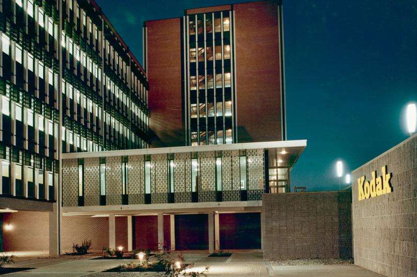 Coloured photo of the Kodak factory, a modernist architectural building, at night, with the lights inside the building glowing