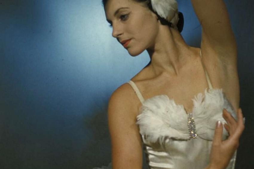 Photo of a ballerina in a white tutu posing with one arm up over her head
