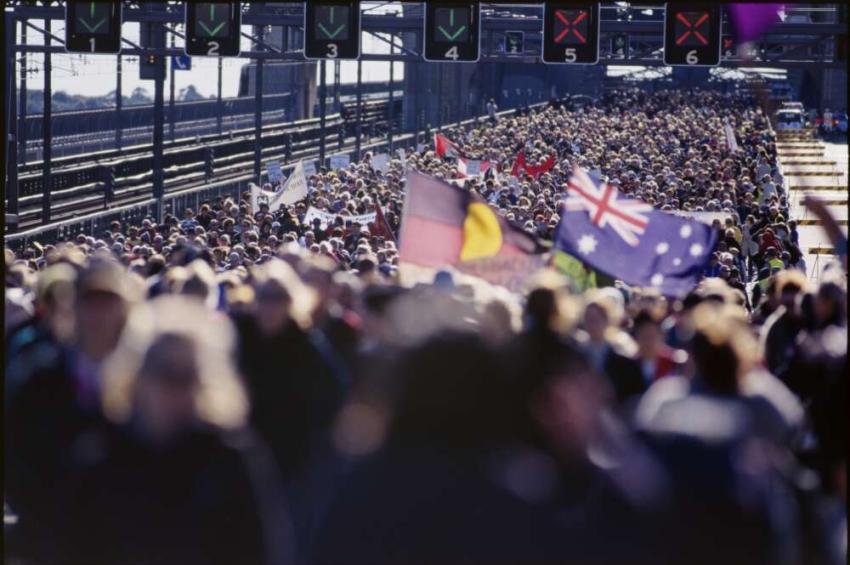 Sydney Harbour Bridge crowded with people, with Aboriginal and Australian flags being held up