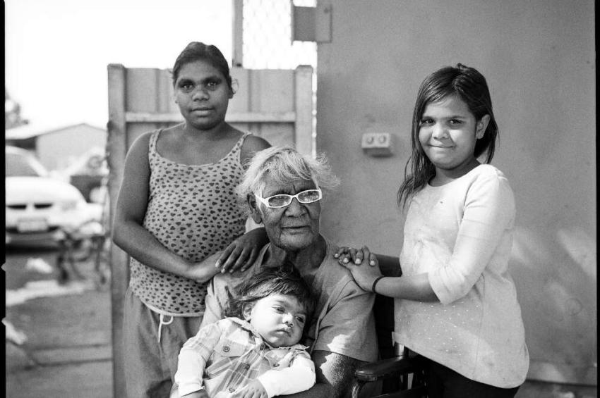 Black and white photo of a First Nations woman in a wheelchair with three of her young grandaughters, two standing behind her one sitting on her lap