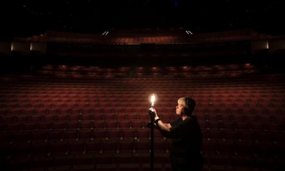 A person stands in an empty darkened theatre, illuminated by a single light bulb.
