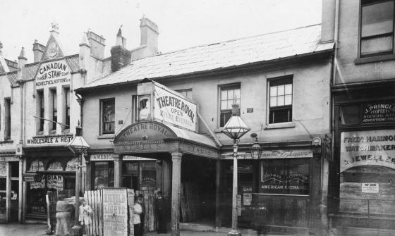 Black and white photograph of a row of shopfronts. One facade reads 'Theatre Royal: Open Every Evening'.