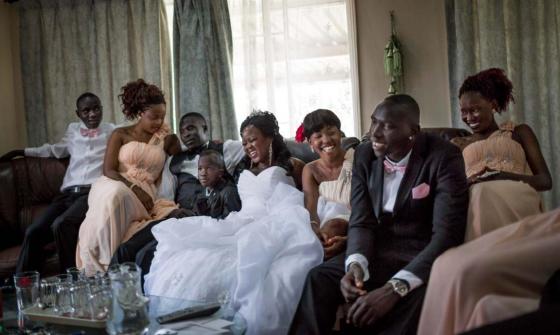 A family dressed for a wedding laughs as they sit together on a couch