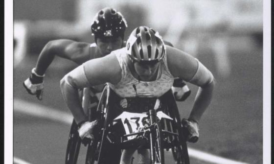 A black and white photo of Louise Sauvage leading another wheelchair racer on a track.